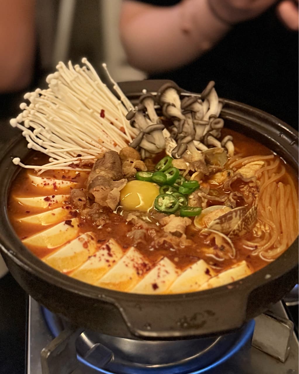 대구광역시 북구 새로나 대구 기타 매장 다찌석 1인 혼술 전골. 조명 아래 팽이버섯, 느타리버섯, 두부, 계란 노른자가 담긴 붉은 육수가 가스레인지 위에서 가열되는 상태.