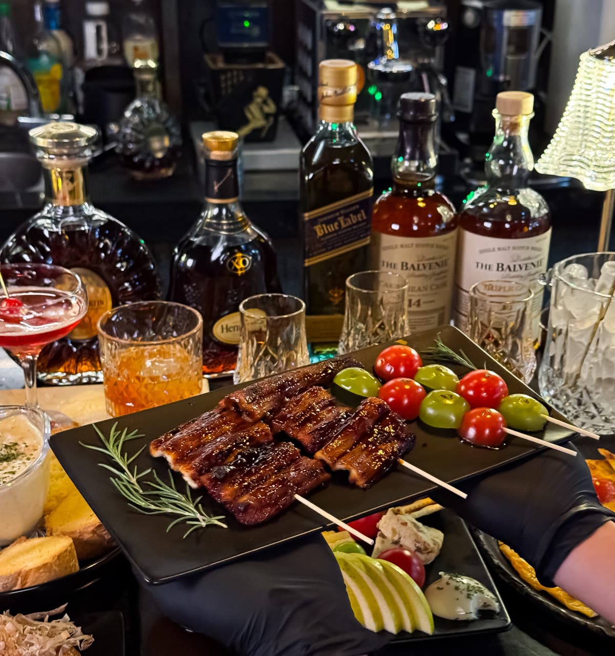 인천광역시 연수구 더킹스 송도술집 인천 바(Bar) 다찌석 혼술. 전등 아래 윤기 흐르는 장어구이와 과일 꼬치 접시 뒤로 위스키 병이 진열된 1인 카운터석.