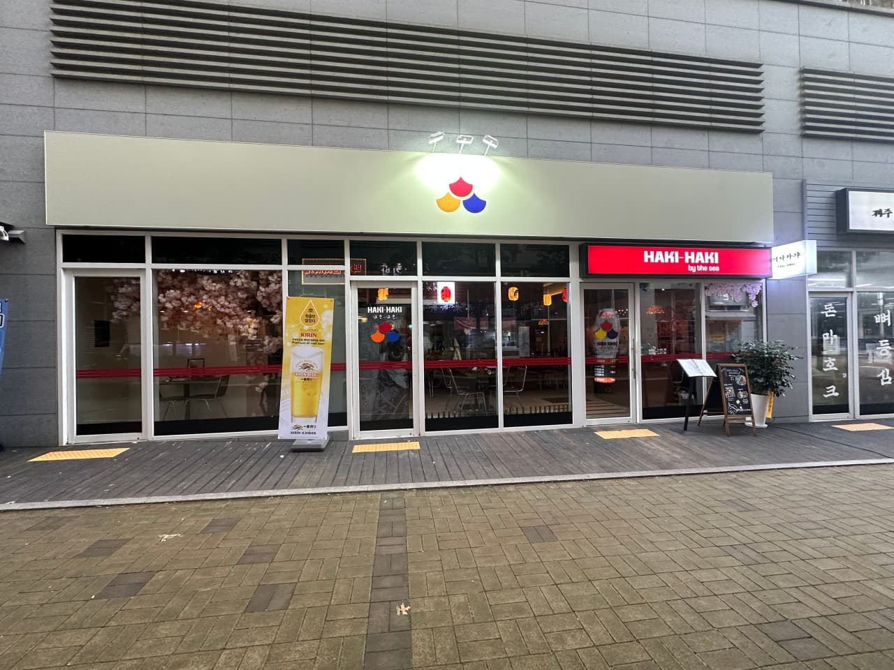 인천광역시 영종구 하키 하키 인천 매장 입구. 밝은 조명 아래 벚꽃과 붉은 제등이 설치된 통유리 너머 1인 혼술 다찌석과 기타 좌석이 배치됨.