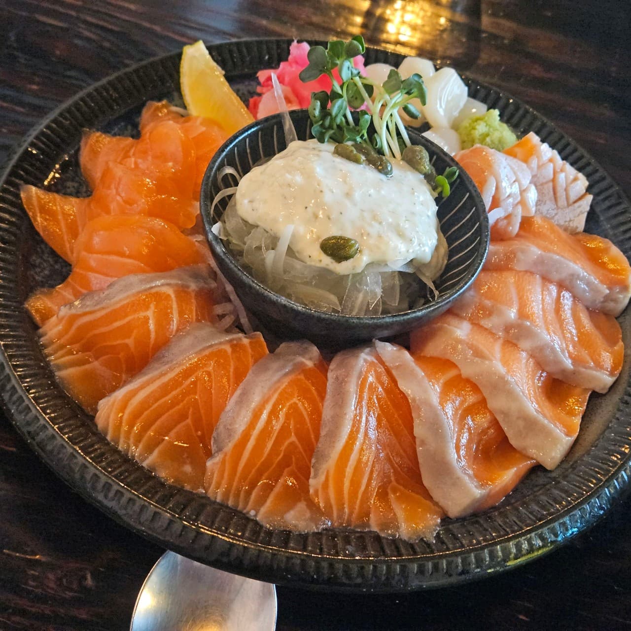 인천광역시 서해구 이고식당 인천 이자카야 다찌석 조명 아래 차려진 1인 연어 사시미. 윤기 흐르는 연어회와 타르타르 소스, 무순, 레몬이 검은 식기에 담겨 혼술 상황을 연출함.