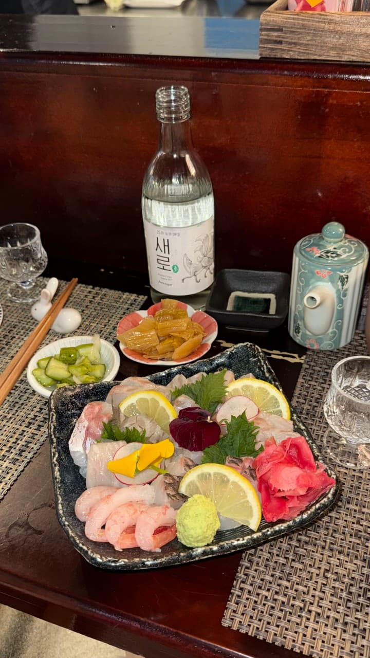 인천광역시 부평구 심야식당 곳간 인천 이자카야의 나무 다찌석 위 1인 사시미 모듬과 소주. 은은한 조명 아래 신선한 회의 질감이 돋보이는 혼술 상황을 묘사함.