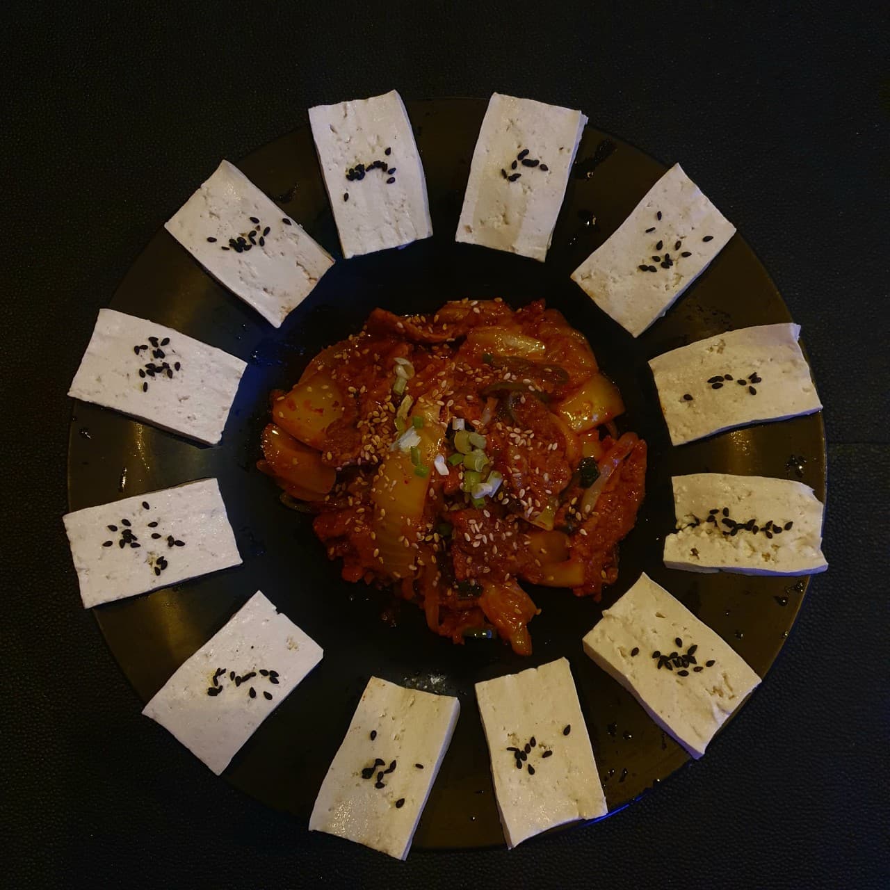 인천광역시 영종구 촤랑 인천 요리주점의 어두운 조명 아래 놓인 두부김치. 원형으로 배치된 두부와 볶음김치가 1인 혼술 안주로 다찌석에 차려짐.