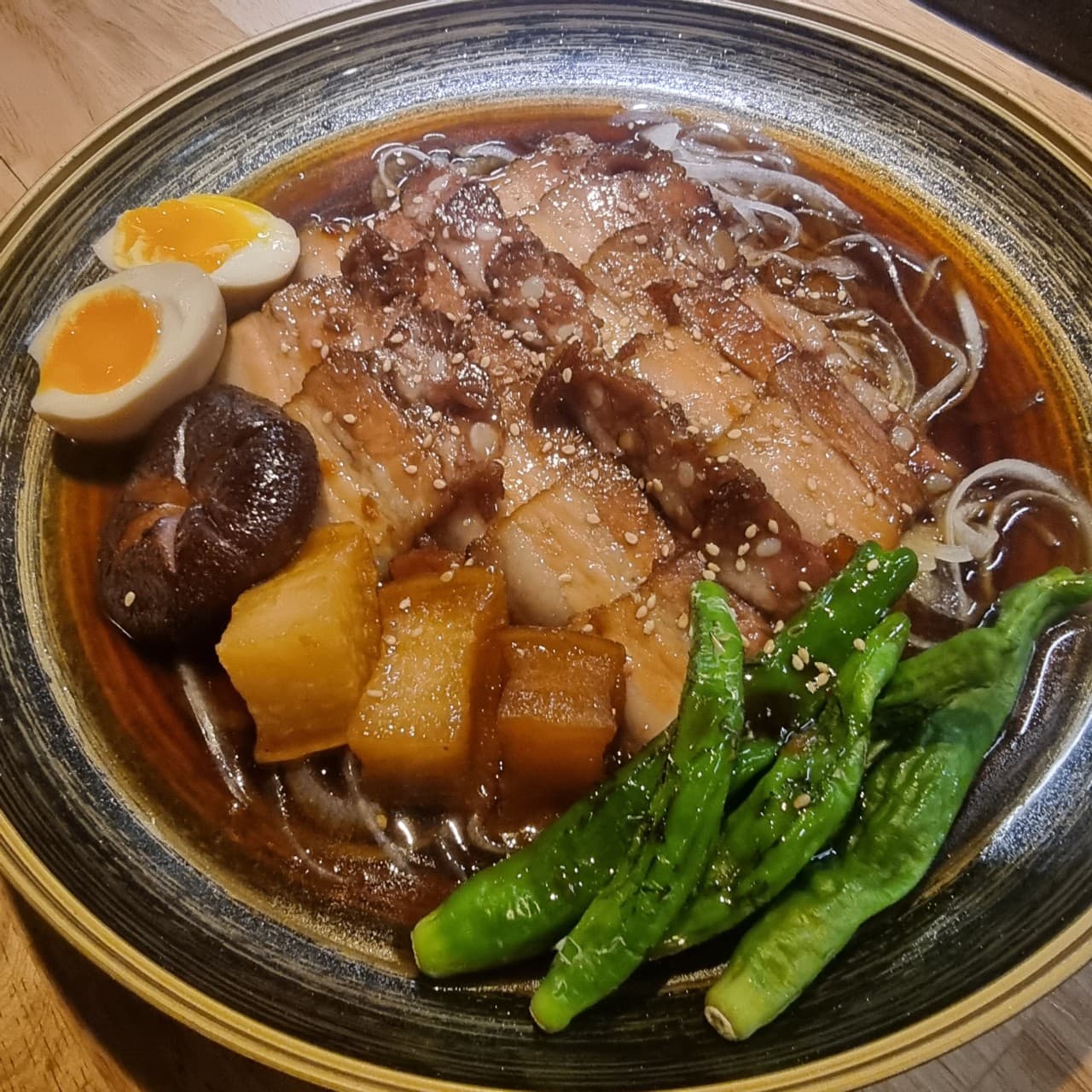 제주특별자치도 제주시 야해 제원노형점 제주 이자카야 다찌석 1인 혼술. 조명 아래 윤기 나는 돼지고기 조림과 꽈리고추, 표고버섯, 반숙 달걀이 담긴 목재 테이블 위 상차림.