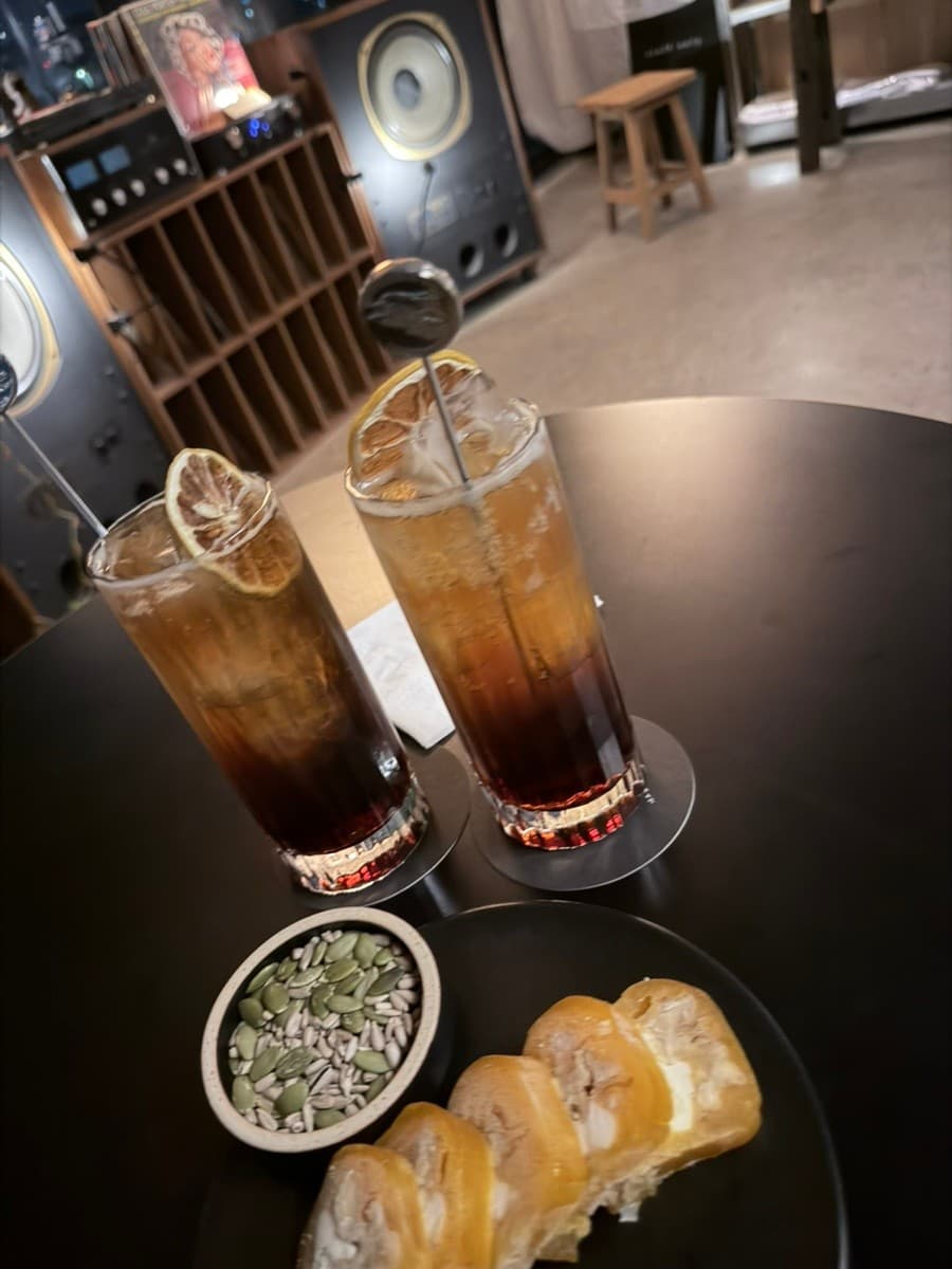 제주특별자치도 제주시 내도음악상가 제주 와인바 어두운 조명 아래 1인 탁자. 탄산 기포가 보이는 하이볼과 부드러운 곶감 치즈 말이, 견과류가 차려진 혼술 상황의 시각적 구성.