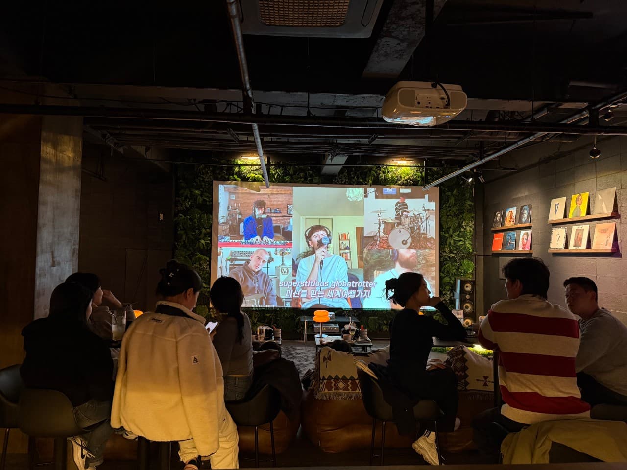 제주특별자치도 서귀포시 1인 혼술 기타 튠:TUNED 제주 - 낮은 조명 아래 다찌석에서 음료와 함께 대형 스크린을 시청하는 상황과 벽면 LP 전시
