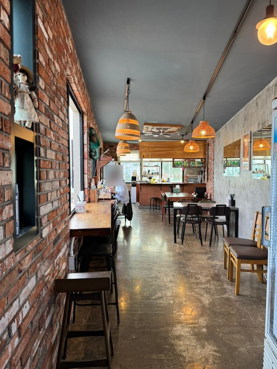 제주특별자치도 서귀포시 통발 성산점 제주 붉은 벽돌과 라탄 조명 아래 길게 배치된 1인 다찌석. 창가 쪽 나무 테이블에 앉아 혼술을 즐기는 상황.