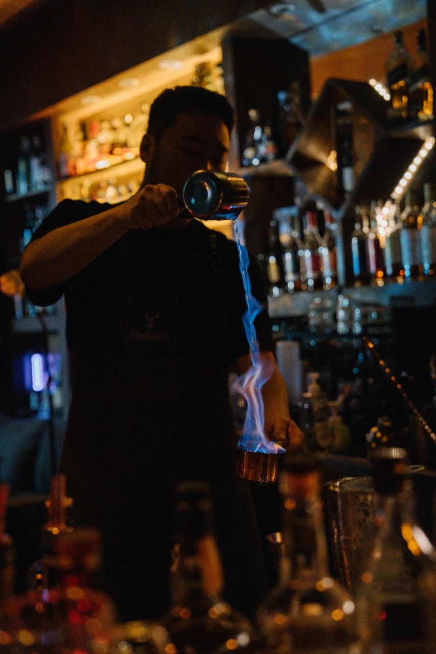 제주특별자치도 서귀포시 혼술바 고도 서귀포점 제주 바(Bar) 다찌석 앞 바텐더가 푸른 불꽃이 이는 칵테일을 따르는 1인 혼술 상황