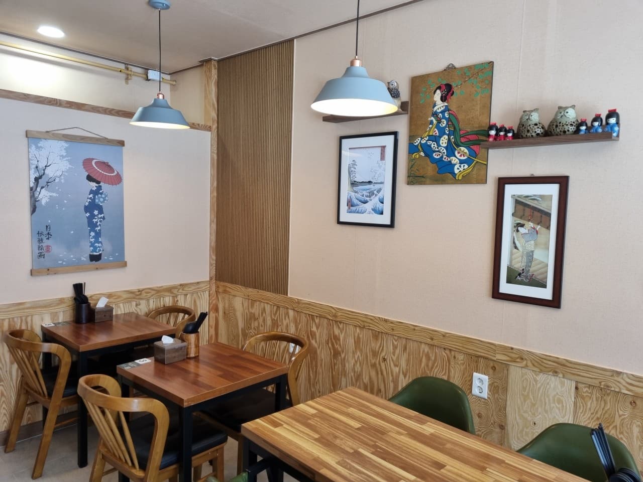 울산광역시 남구 혼술 이자카야 고꼬 - 일본풍 민화와 소품이 배치된 벽면 아래 나무 소재 테이블과 조명이 설치된 1인 및 다인용 좌석 공간