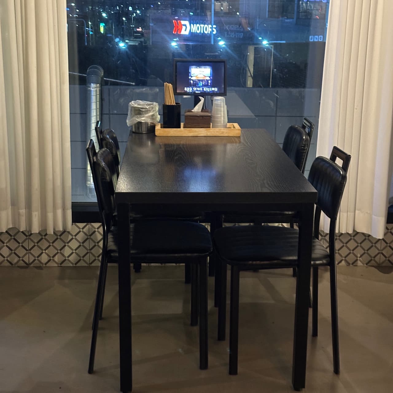 울산광역시 북구 이자카야 오사카로맨스 매곡점 창가석. 검은색 목재 테이블과 태블릿 메뉴판이 배치되었으며 통창 너머 야경이 비치는 1인 혼술 좌석 환경.