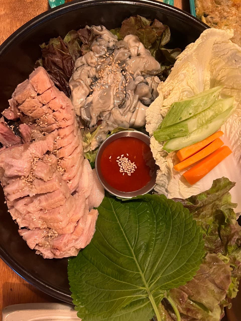 강원특별자치도 속초시 청학동사거리 전통주점의 노란 조명 아래 차려진 1인 굴보쌈 세트. 나무 테이블 위 수육과 생굴, 쌈 채소가 담긴 접시로 혼술 상황을 연출함.