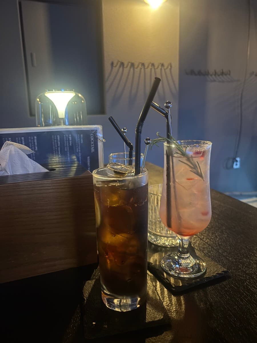 강원특별자치도 강릉시 혼술바 파도끝 바(Bar) 다찌석 위 칵테일. 노란 조명 아래 얼음과 로즈마리가 담긴 유리잔이 놓인 1인 혼술 상황.