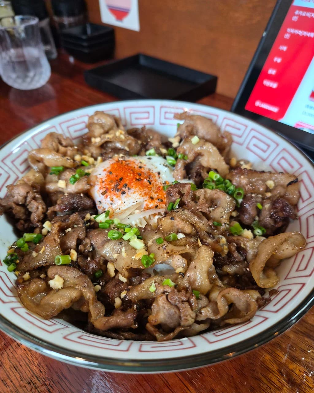 강원특별자치도 원주시 이자카야 카도야의 다찌석 1인 식사. 반숙란과 고춧가루가 뿌려진 고기 덮밥의 질감과 나무 테이블 위 태블릿 메뉴판이 놓인 혼술 상황.