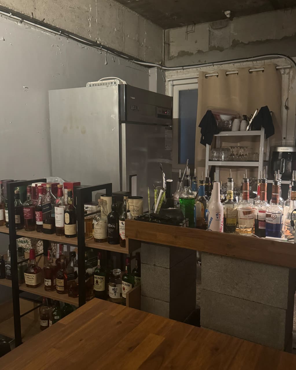 강원특별자치도 강릉시 주인 강릉혼술바 강릉점 바(Bar) 내부. 낮은 조도의 조명 아래 원목 테이블과 다찌석이 배치되어 있고 위스키 병들이 진열된 혼술 상황.