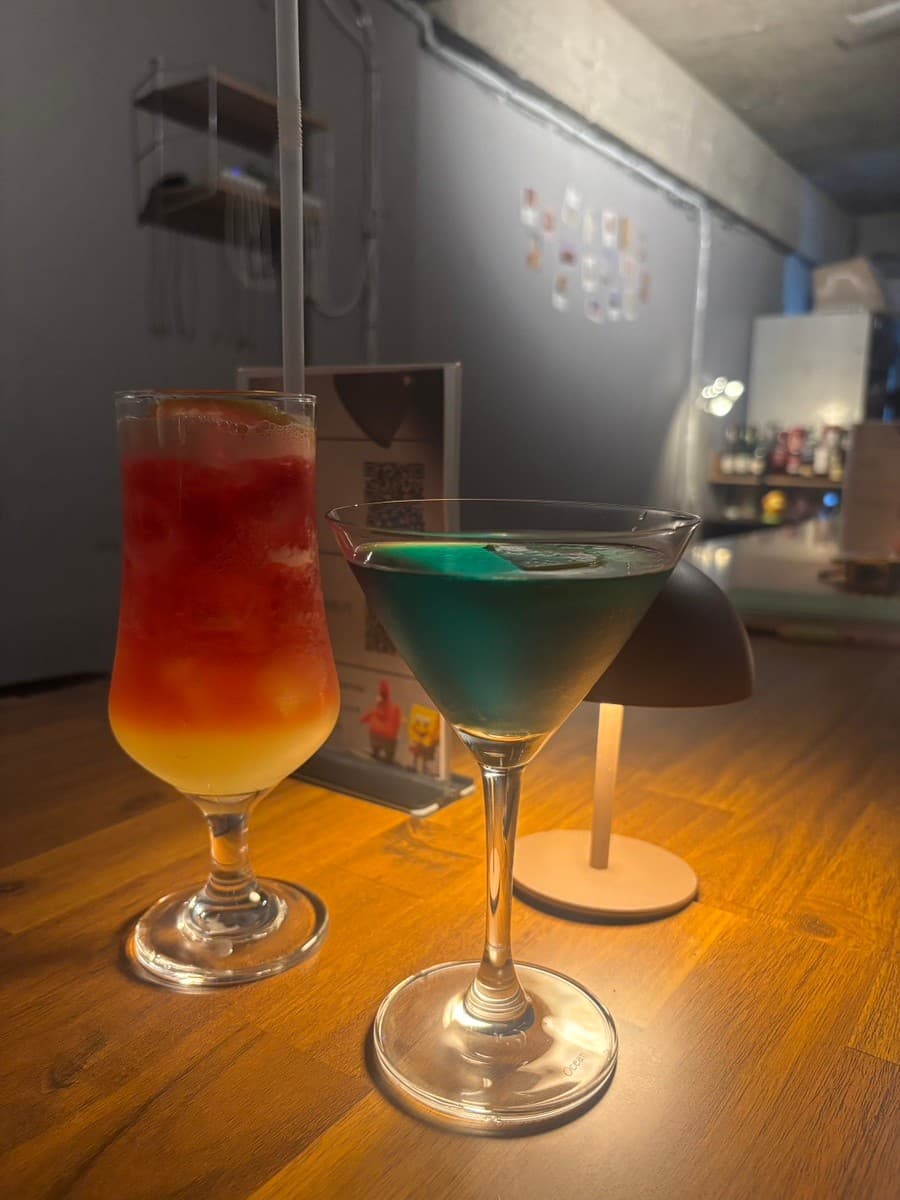 강원특별자치도 강릉시 주인 강릉혼술바 강릉점 바(Bar) 다찌석 조명 아래 놓인 빨간색과 파란색 칵테일. 1인 혼술을 위해 어둡게 조성된 내부와 나무 테이블의 질감이 나타남.