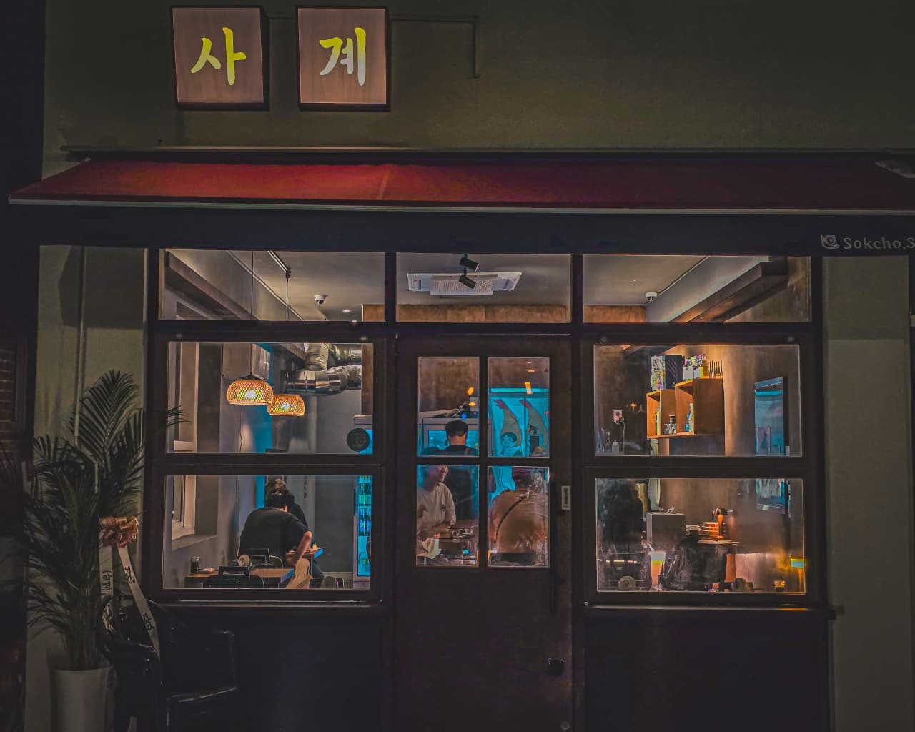 강원특별자치도 속초시 요리주점 속초사계 - 노란 조명 아래 다찌석에서 혼술하는 사람들과 목재 인테리어가 보이는 매장 정면 외관