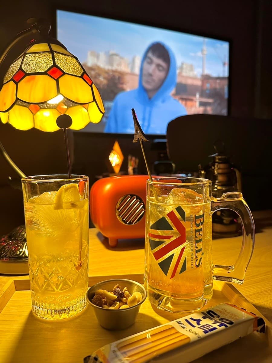 강원특별자치도 강릉시 라면먹고갈래 관동별곡 노란 조명 아래 하이볼과 견과류가 차려진 혼술 테이블. 기타 메뉴와 함께 영상을 즐기는 1인석의 시각적 요소.