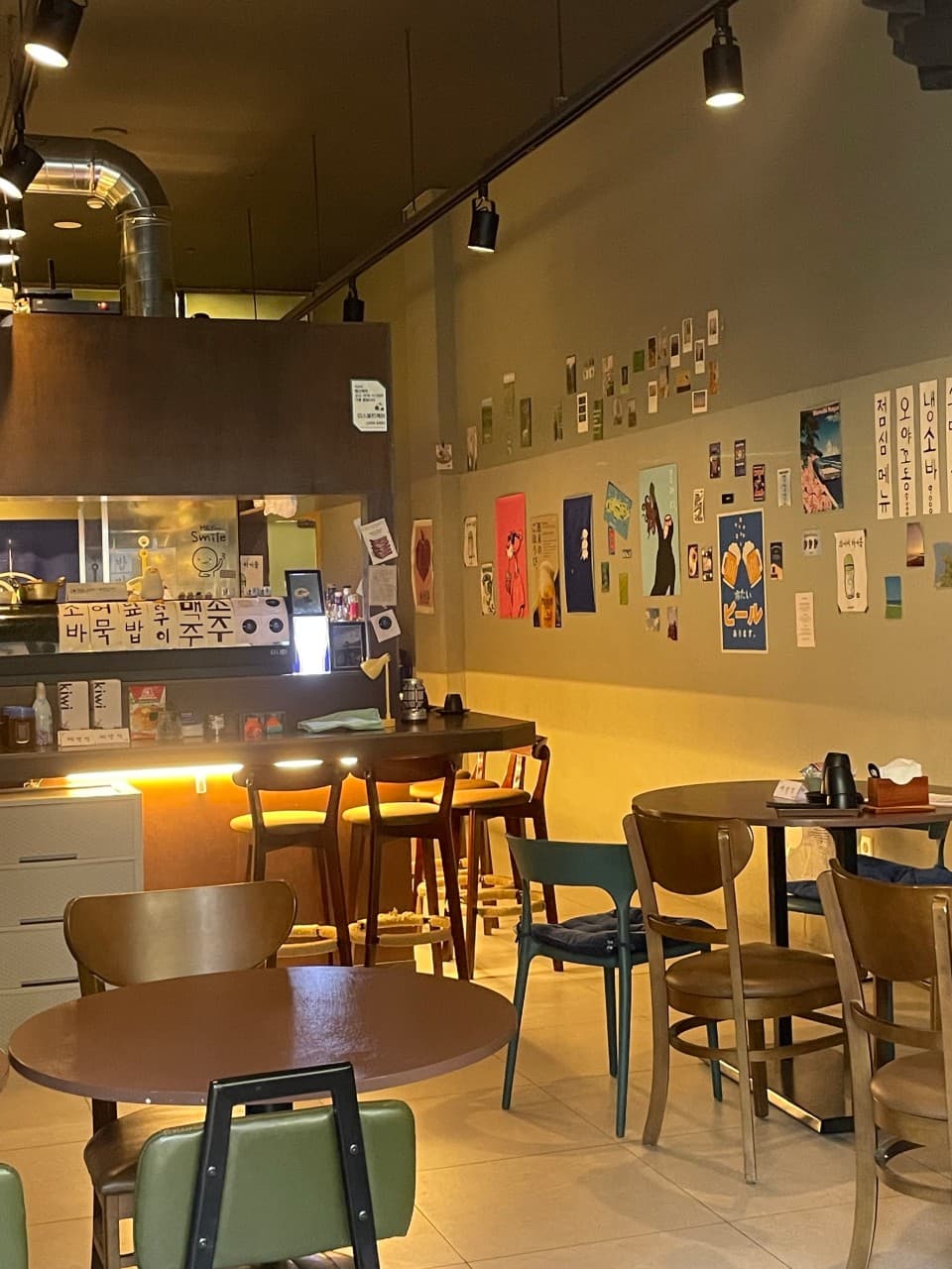 강원특별자치도 원주시 오뎅바 육지놈들 내부의 노란 레일 조명이 비추는 1인 다찌석과 포스터가 부착된 벽면 아래 원형 테이블이 배치된 혼술 공간