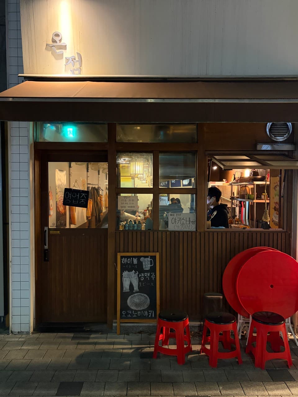 강원특별자치도 원주시 온점 이자카야 - 노란 조명 아래 다찌석이 보이는 목재 외관과 야키소바빵 메뉴, 빨간 의자가 배치된 혼술 공간