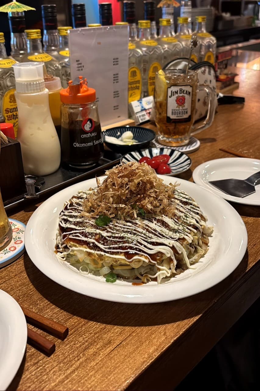 강원특별자치도 원주시 온점 이자카야 다찌석 혼술. 가쓰오부시가 얹어진 오코노미야키와 하이볼이 놓인 목재 카운터 위로 조명이 비치며 위스키 병들이 나열됨.