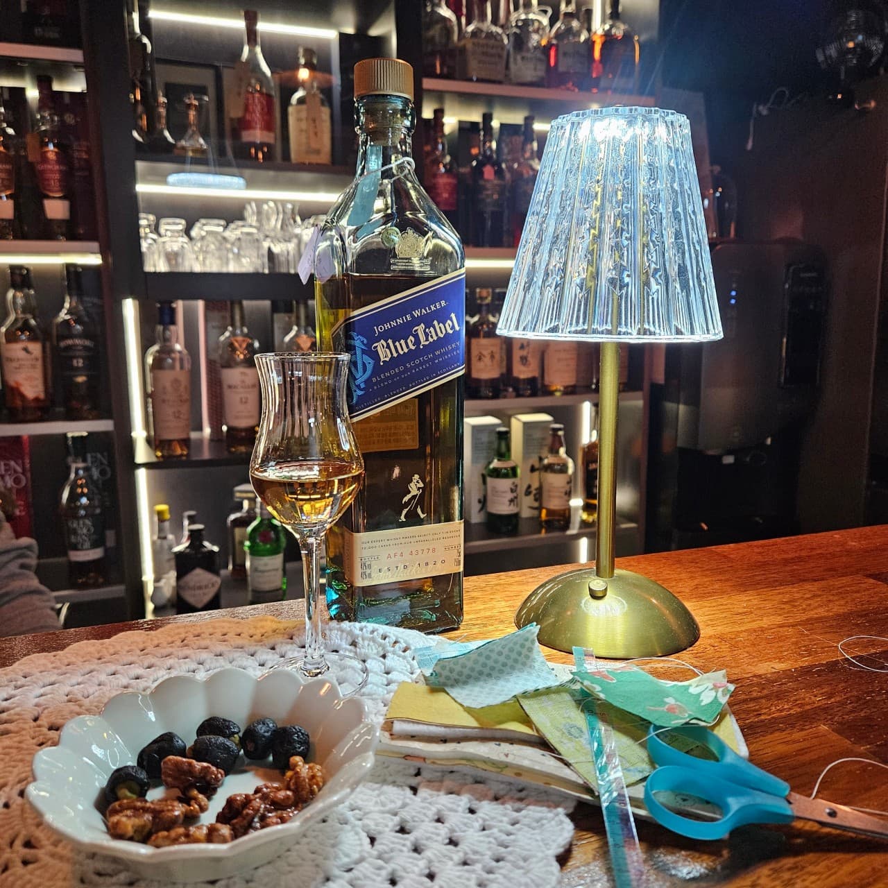 강원특별자치도 철원군 쁘띠클로젯 사사로운공간 바(Bar) - 조명 켜진 1인 다찌석 위 위스키와 견과류, 바느질 소품이 놓인 혼술 상황
