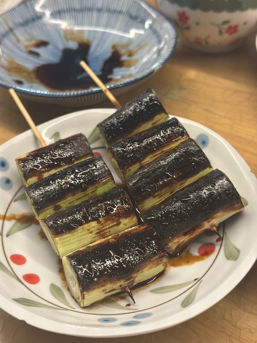 강원특별자치도 원주시 이자카야 히바나 다찌석에서 즐기는 혼술. 나무 테이블 위 윤기 나는 소스가 발린 대파 구이 꼬치와 파란 무늬 접시가 놓인 1인 상차림.