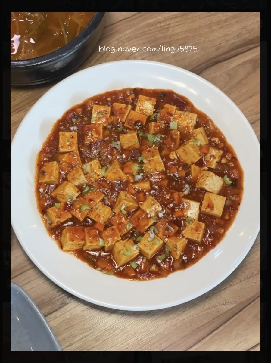 강원특별자치도 속초시 나이스포차 포장마차 1인 다찌석에 차려진 마파두부. 나무 테이블 위 조명을 받아 붉은 양념 질감이 선명한 안주와 국물이 놓인 혼술 차림.