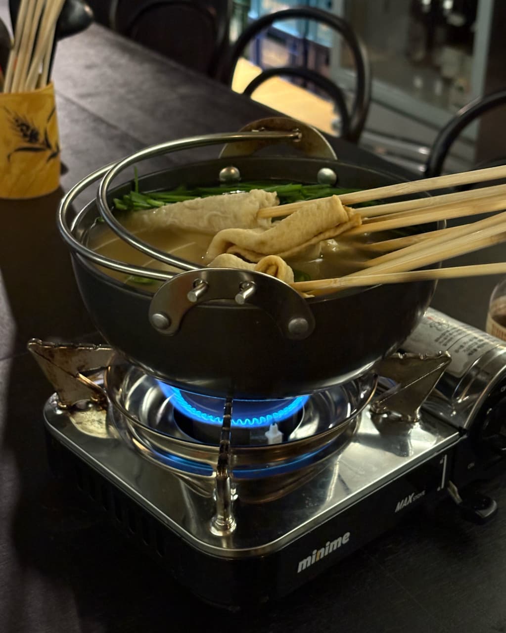 강원특별자치도 춘천시 감마샵앤바 혼술 - 휴대용 버너의 파란 불꽃 위에서 끓고 있는 꼬치 어묵탕과 어두운 조명 아래의 1인 다찌석