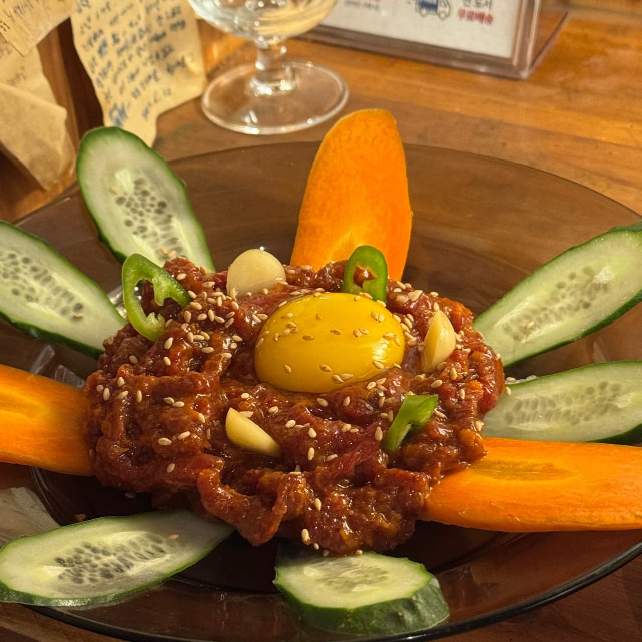 강원특별자치도 속초시 요리주점 아프리카 다찌석 조명 아래 노른자와 깨가 뿌려진 매콤한 질감의 고추장 육회. 오이와 당근이 정갈하게 놓인 1인 안주로 혼술하는 상황.