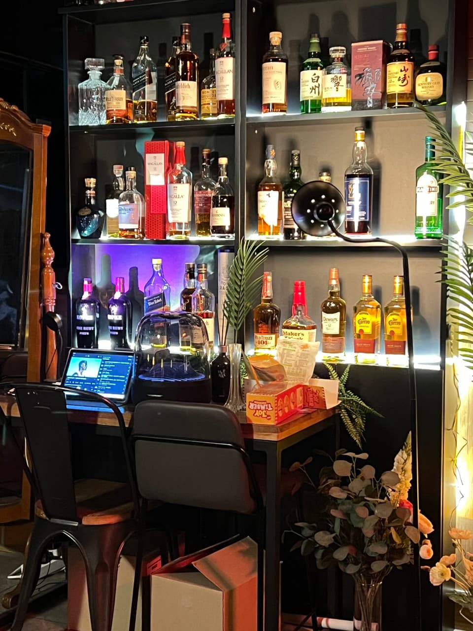 강원특별자치도 원주시 라벨라다 바(Bar)의 조명 아래 배치된 위스키 진열장과 1인 테이블. 태블릿과 안주가 놓인 다찌석에서 혼술을 즐기는 상황.