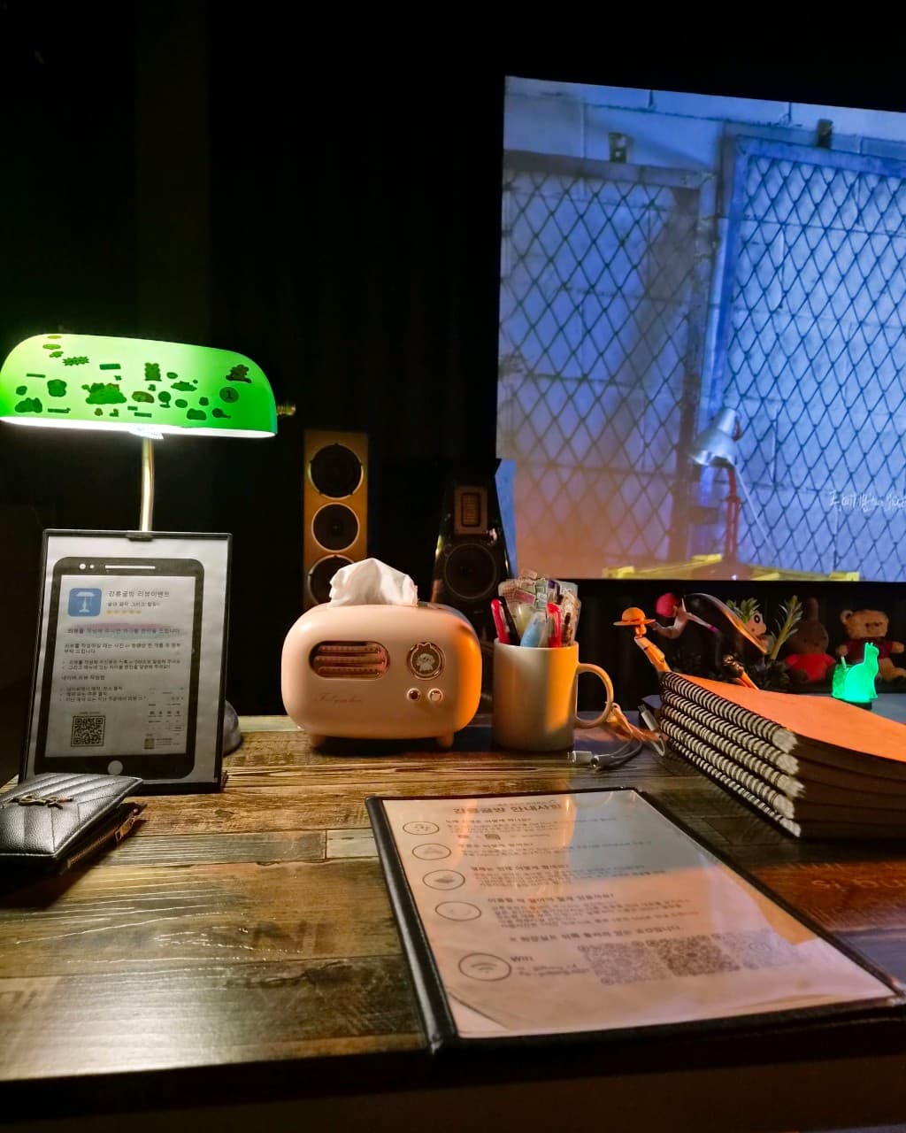 강원특별자치도 강릉시 강릉골방 와인바의 1인 다찌석. 초록색 조명 아래 놓인 노트와 필기구, 대형 스크린이 있는 어두운 실내에서 혼술을 즐기는 상황.
