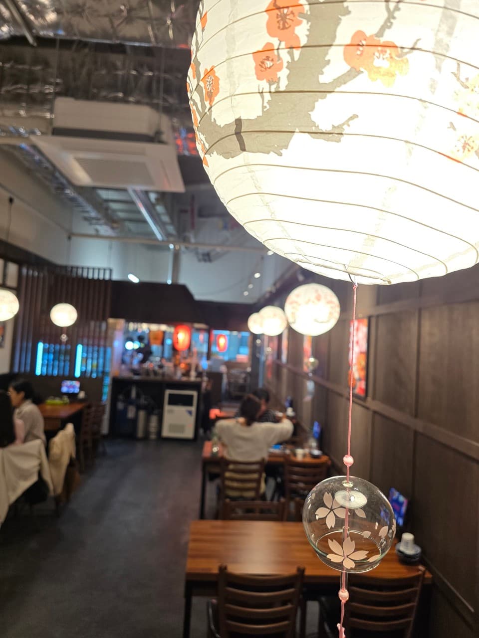 세종특별자치시 대평3길 요리주점 타코로 세종대평점. 벚꽃 문양 종이 전등 아래 나무 테이블과 다찌석이 배치되어 혼술하기 적합한 1인석 공간을 구성함.