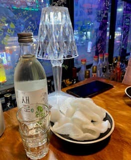 세종특별자치시 나성로 요리주점 지금보고싶다 세종나성점의 창가 다찌석. 크리스탈 조명 아래 소주 한 병과 바삭한 질감의 안주가 차려진 1인 혼술 상황.