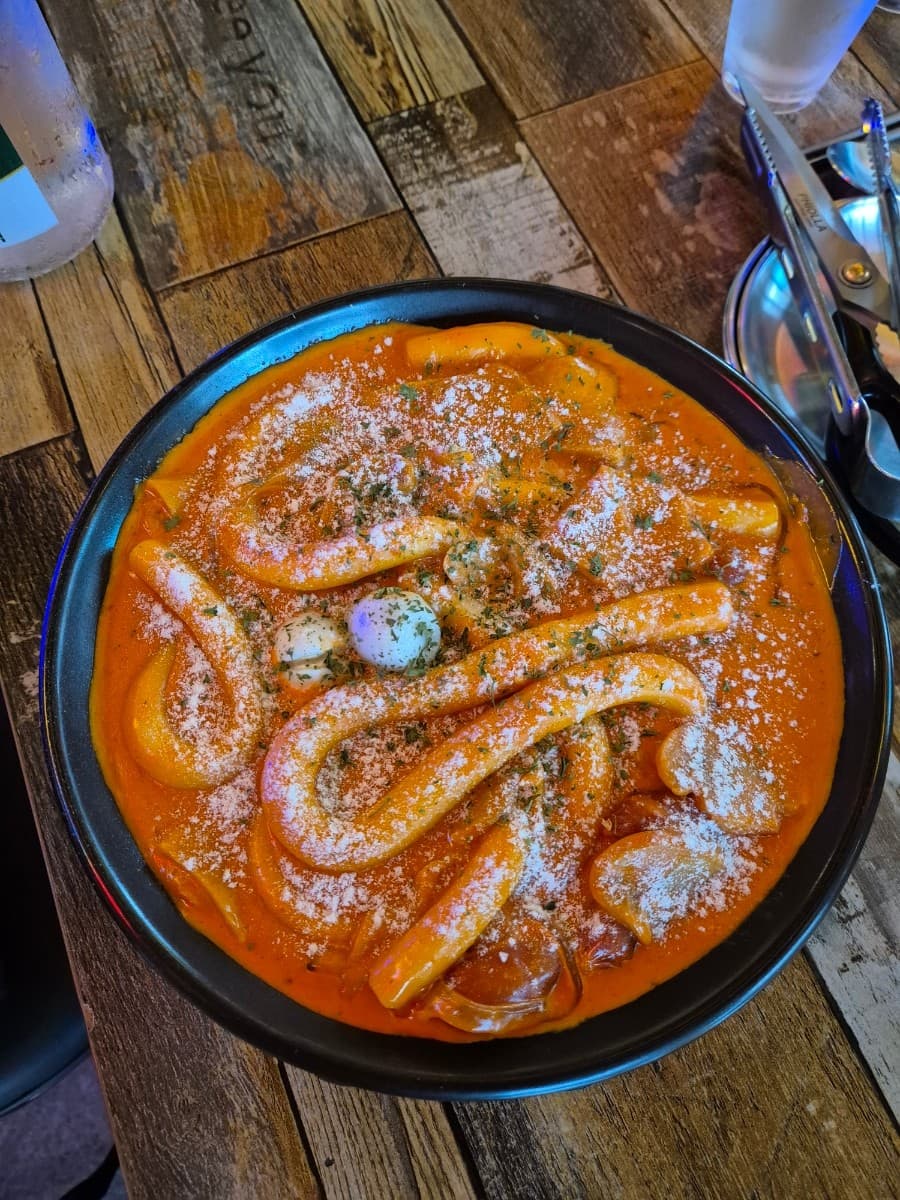 세종특별자치시 해밀3로 무지개맥주 세종해밀점 맥주 호프 1인 혼술. 나무 식탁 위 치즈 가루와 파슬리가 뿌려진 꾸덕한 로제 떡볶이와 집게가 놓인 좌석 상황.