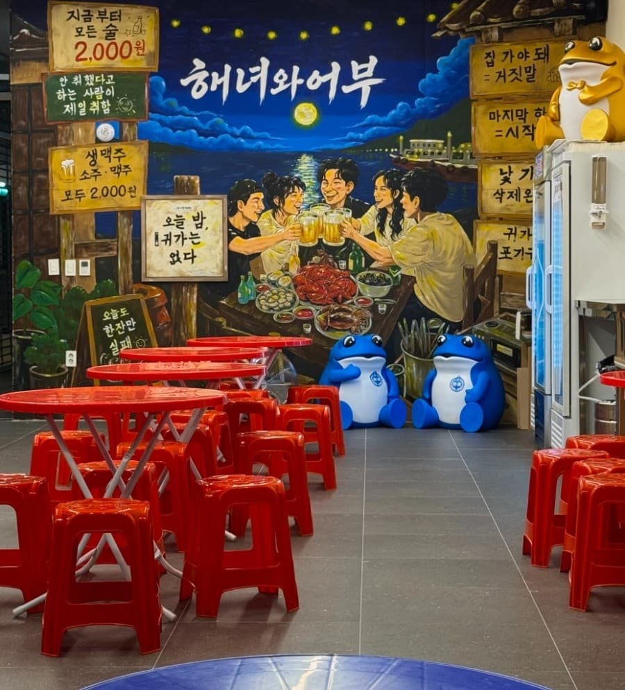 세종특별자치시 나성로 요리주점 해녀와어부 내부의 붉은색 원형 테이블과 간이 의자. 벽면의 인물 벽화와 캐릭터가 배치된 공간에서 혼술을 즐기는 포차 구성.