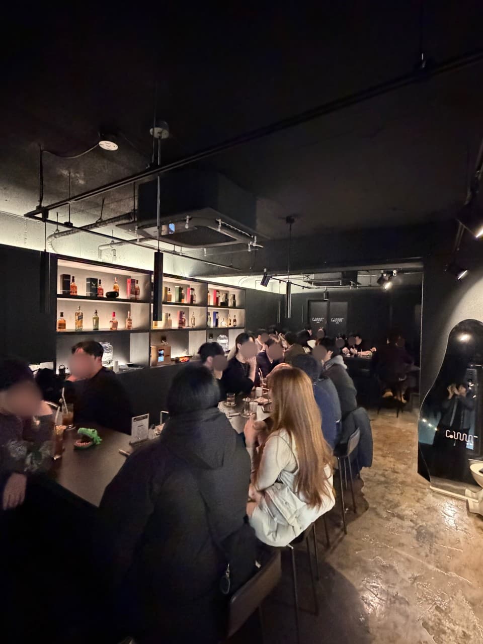경상남도 창원시 꼼바혼술바 창원상남점 바(Bar) 내부. 핀 조명이 비추는 블랙 톤의 1인 다찌석과 벽면 진열장의 위스키병들. 카운터석에 앉아 하이볼을 즐기는 혼술 상황.