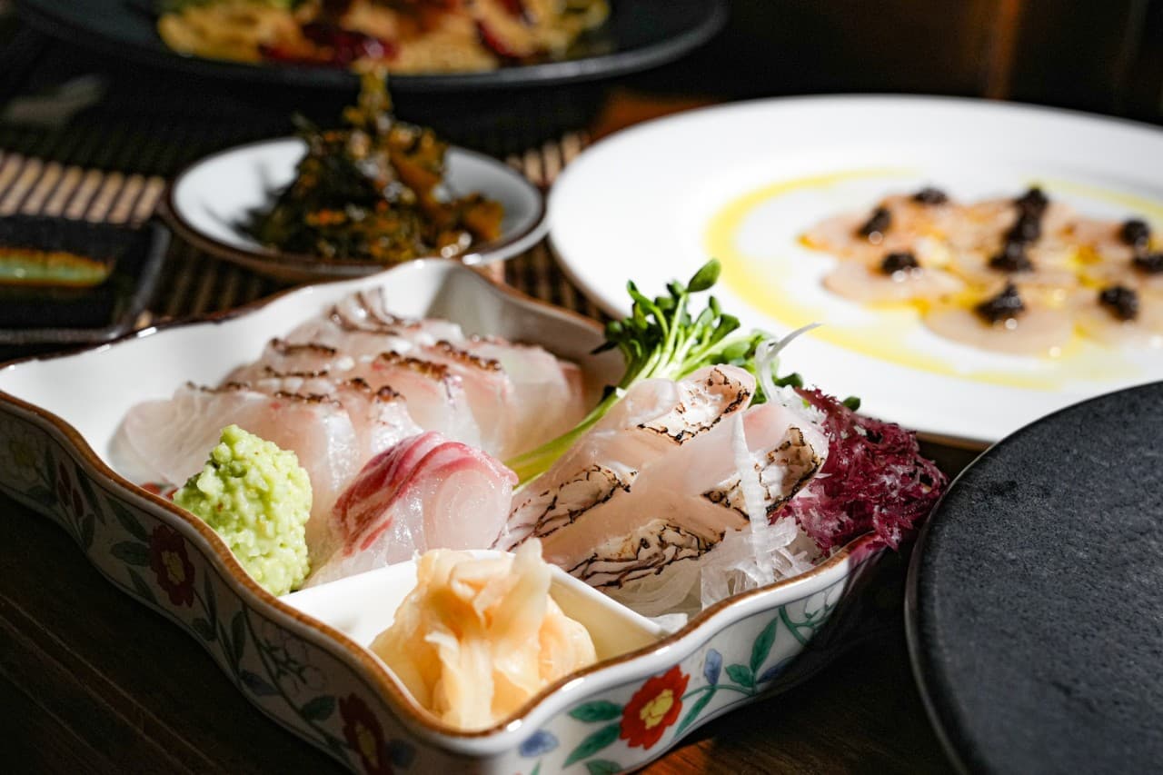 경상남도 창원시 이자카야 삼미정 다찌석 조명 아래 차려진 1인 사시미와 요리. 껍질을 그을린 생선회의 질감과 고추냉이가 강조된 혼술 상황.