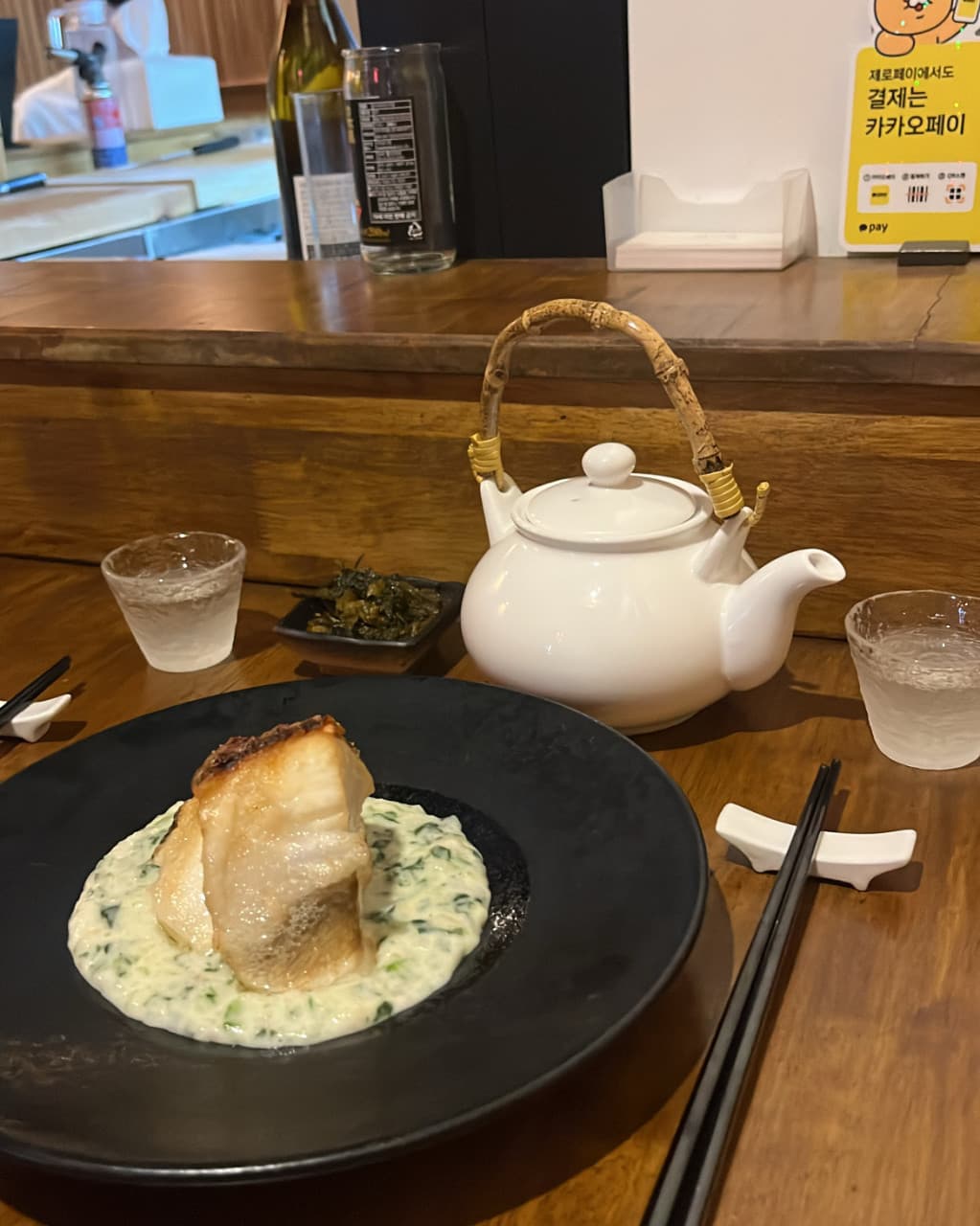 경상남도 창원시 이자카야 삼미정 1인 혼술 다찌석. 조명 아래 크림 소스를 곁들인 생선 구이와 흰색 도자기 주전자가 차려진 상황.