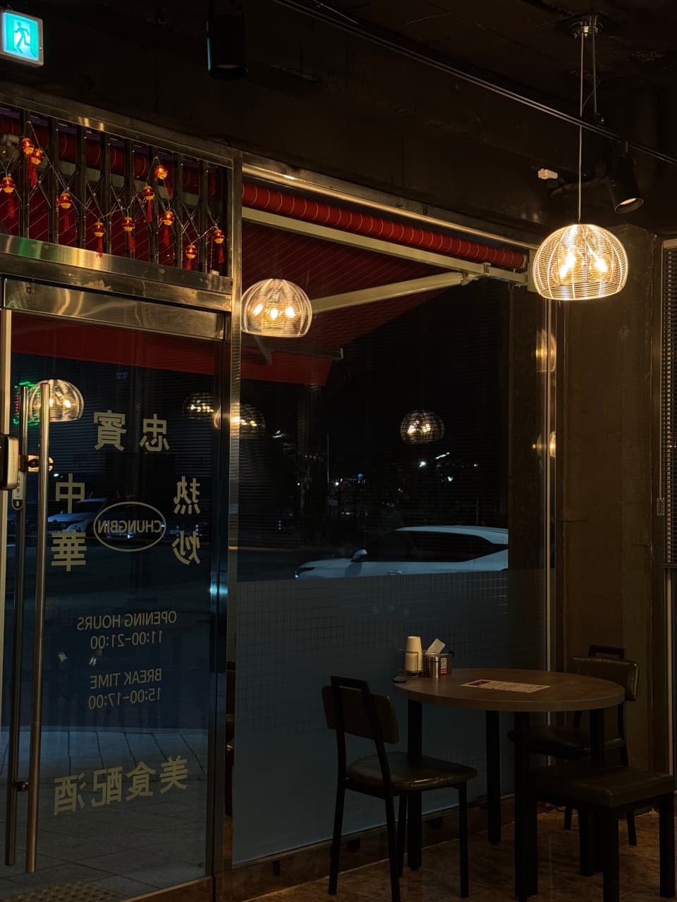 경상남도 진주시 충빈 진주혁신도시점 - 주황색 전등 아래 원형 테이블과 의자가 배치된 1인 혼술 공간. 유리문에 전구 빛이 반사되는 기타 중식 요리 주점 내부.