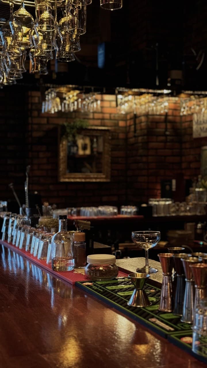 충청북도 음성군 512saloon 펍&바 다찌석에 배치된 칵테일 잔과 바 도구들. 붉은 벽돌 벽면과 조명 아래 혼술을 위해 마련된 1인석 카운터 공간.