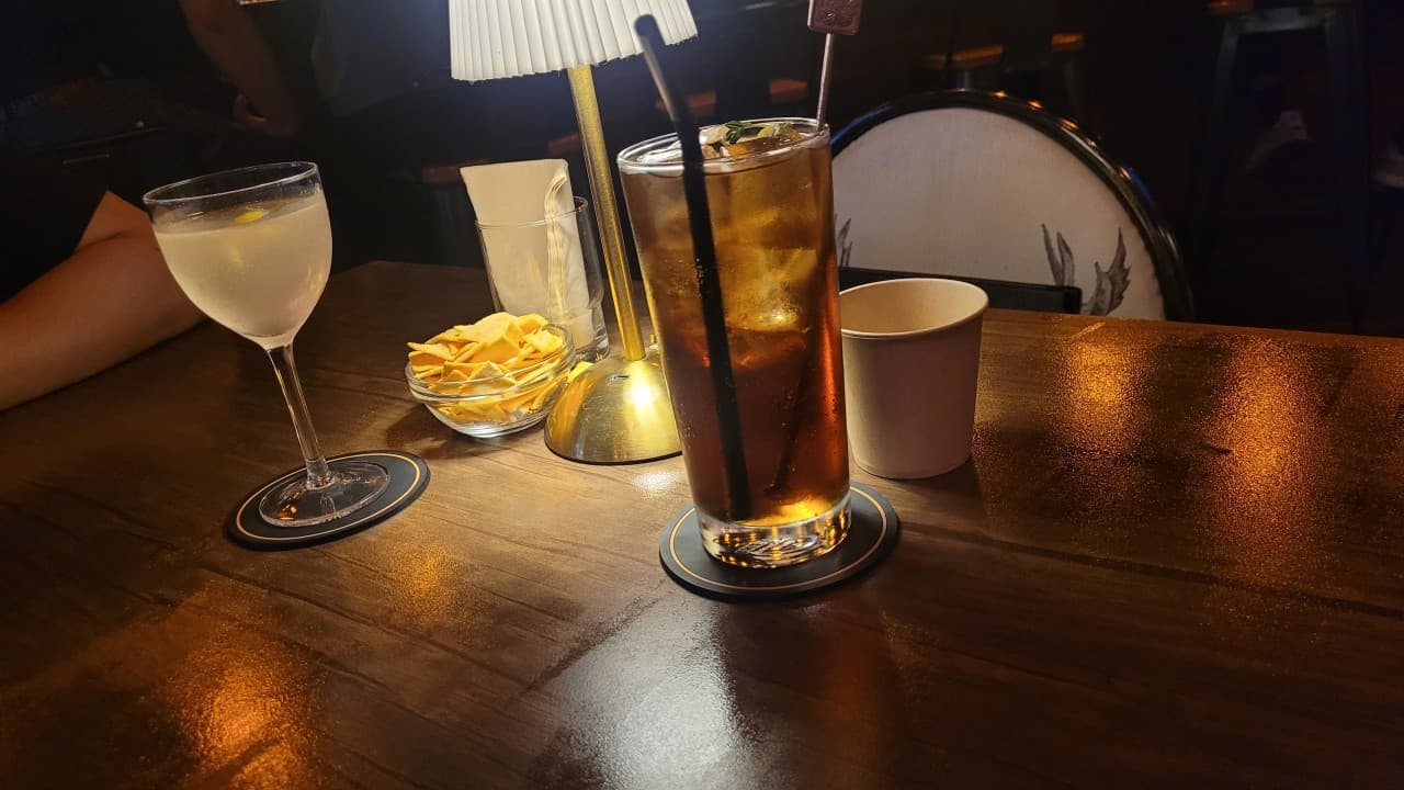 충청북도 음성군 512saloon 펍&바 - 노란 조명 아래 칵테일 두 잔과 기본 안주가 놓인 다찌석에서 즐기는 혼술 상황