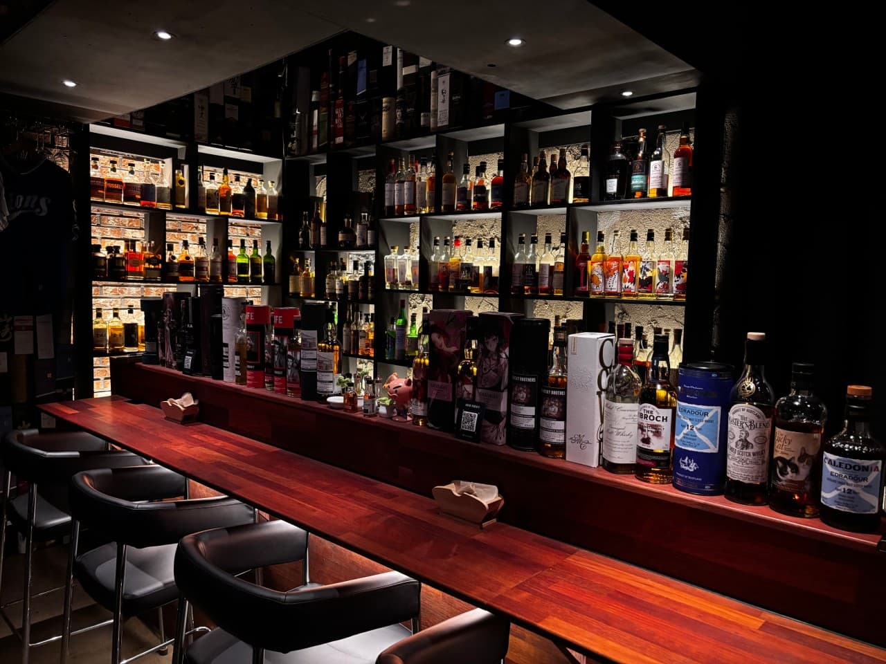 충청북도 청주시 위숙희 바(Bar)의 핀 조명이 비치는 긴 목재 다찌석과 벽면의 다양한 위스키병들. 1인 혼술을 위한 검은색 가죽 좌석이 일렬로 배치된 매장 내부.