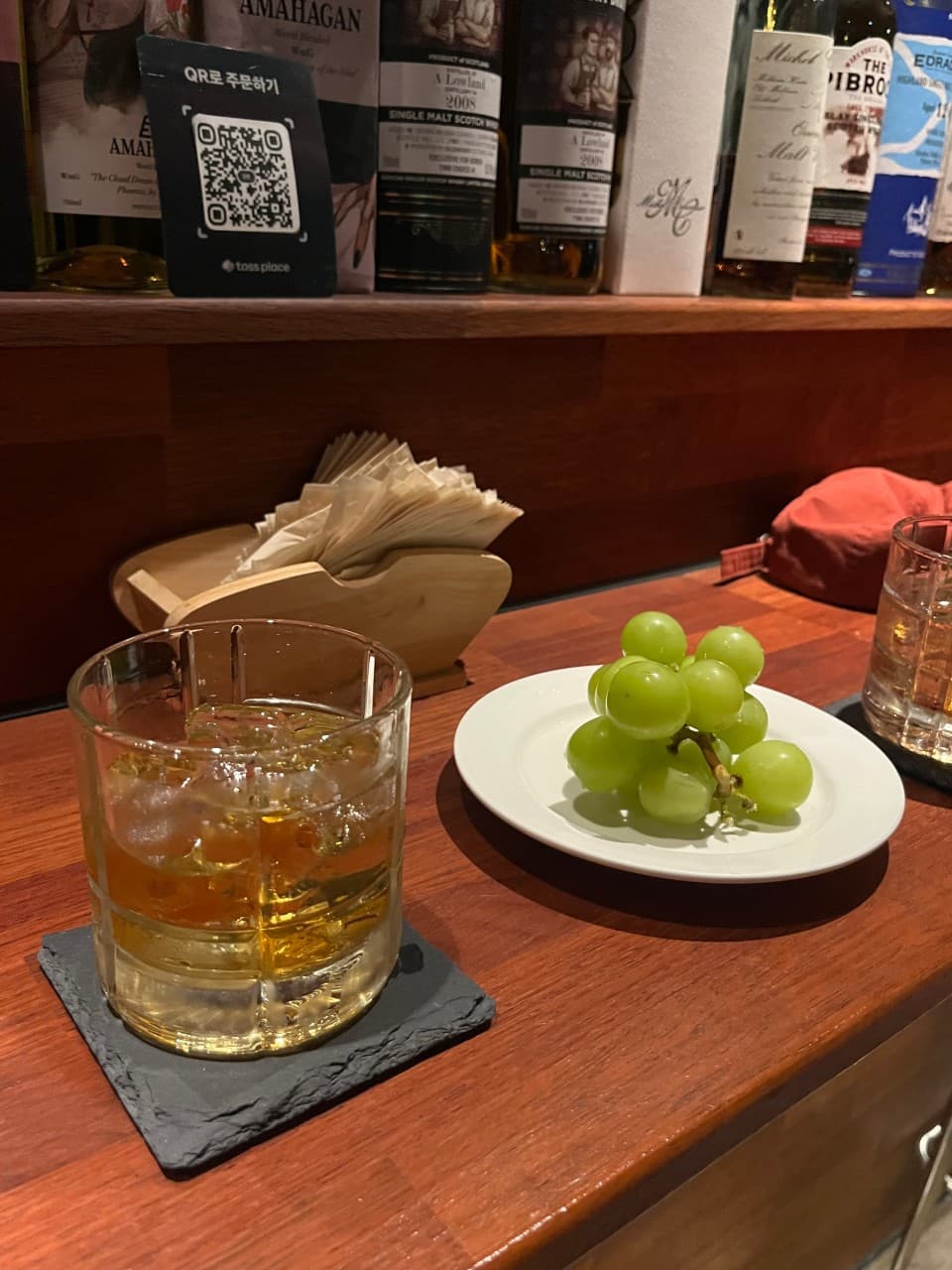 충청북도 청주시 위숙희 바(Bar) 다찌석 위 얼음 담긴 위스키와 청포도. 어두운 조명 아래 나무 카운터에서 1인 혼술을 즐기는 상황.