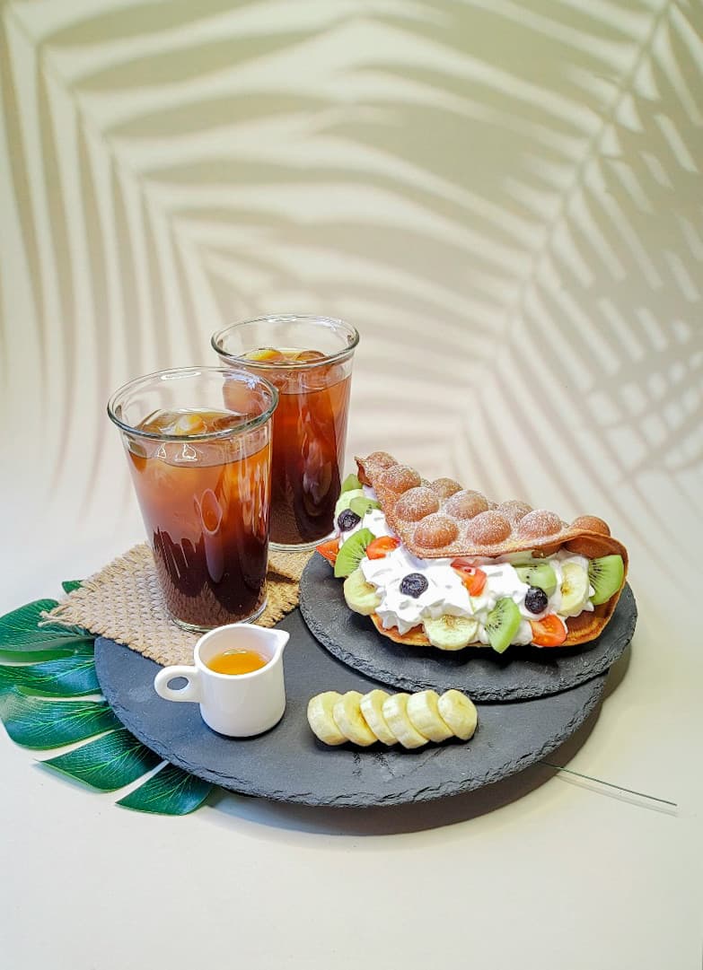 충청북도 청주시 기니쉬커피바 바(Bar) 1인석에 차려진 생크림 과일 홍콩와플과 커피. 잎사귀 그림자 아래 배치된 디저트와 음료의 시각적 질감을 보여주는 상황.
