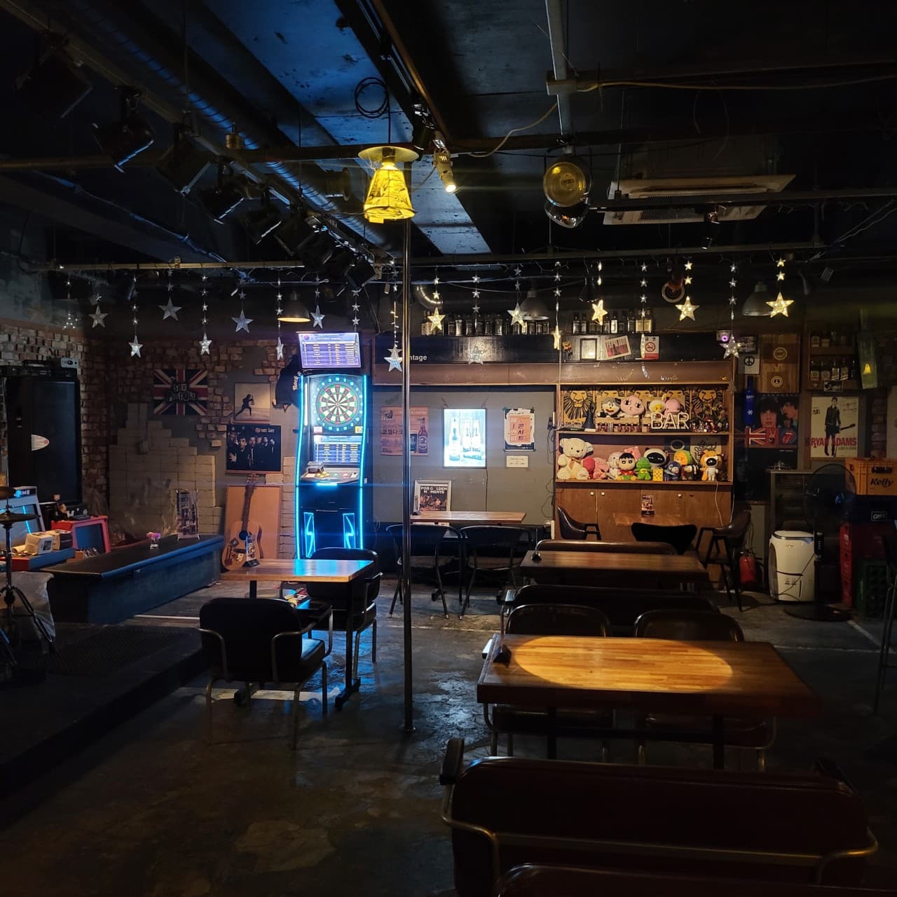 충청북도 청주시 라온 바(Bar) 실내. 노란 핀 조명이 비추는 나무 테이블과 다트 기계, 별 모양 장식등이 배치된 공간에서 즐기는 1인 혼술 상황.