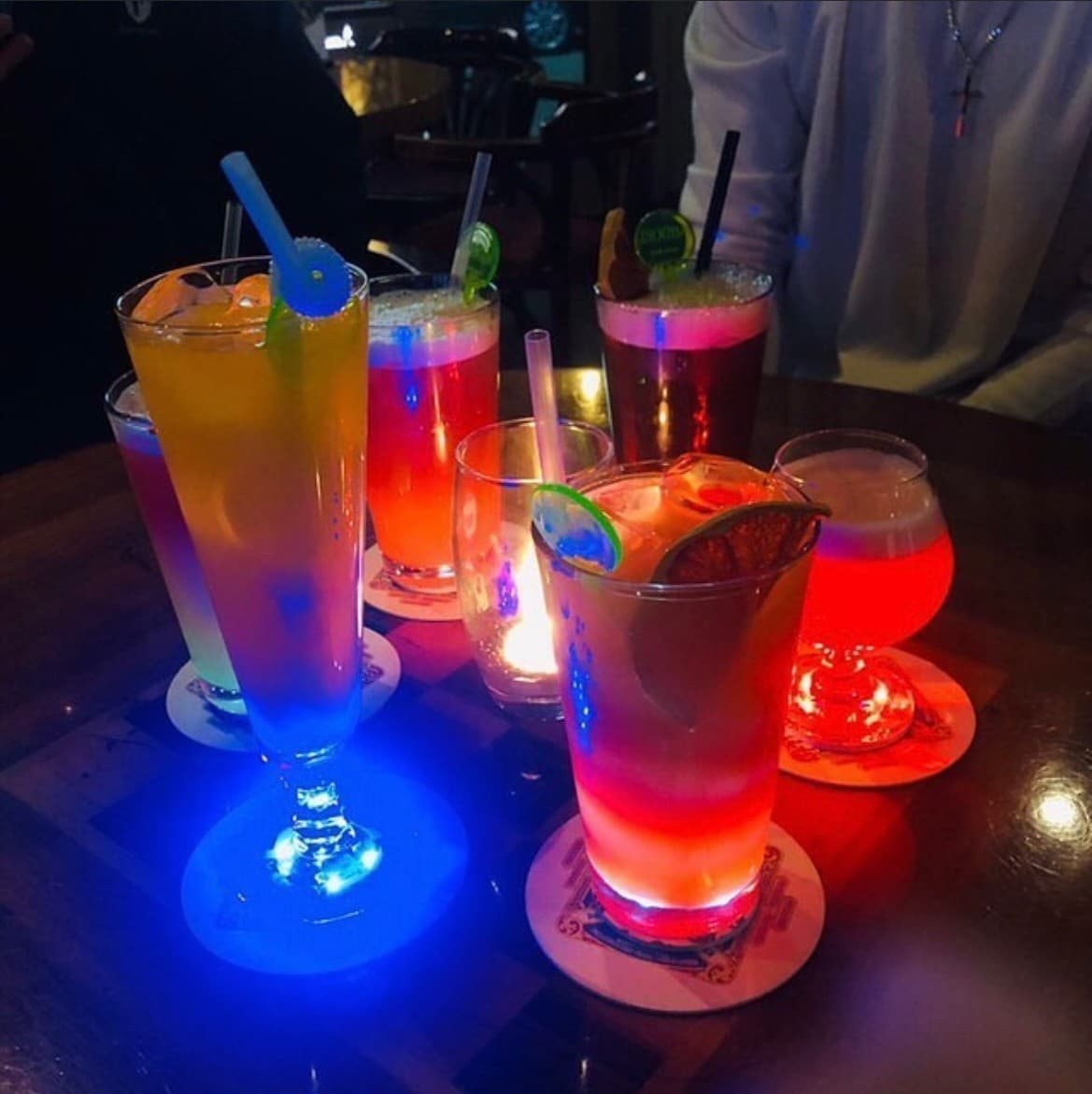 충청북도 제천시 웨스턴빌리지 바(Bar)의 어두운 조명 아래 다찌석에 차려진 1인 혼술 칵테일. 파란색과 빨간색으로 빛나는 컵받침 위로 투명한 얼음과 과일 장식의 질감이 강조됨.
