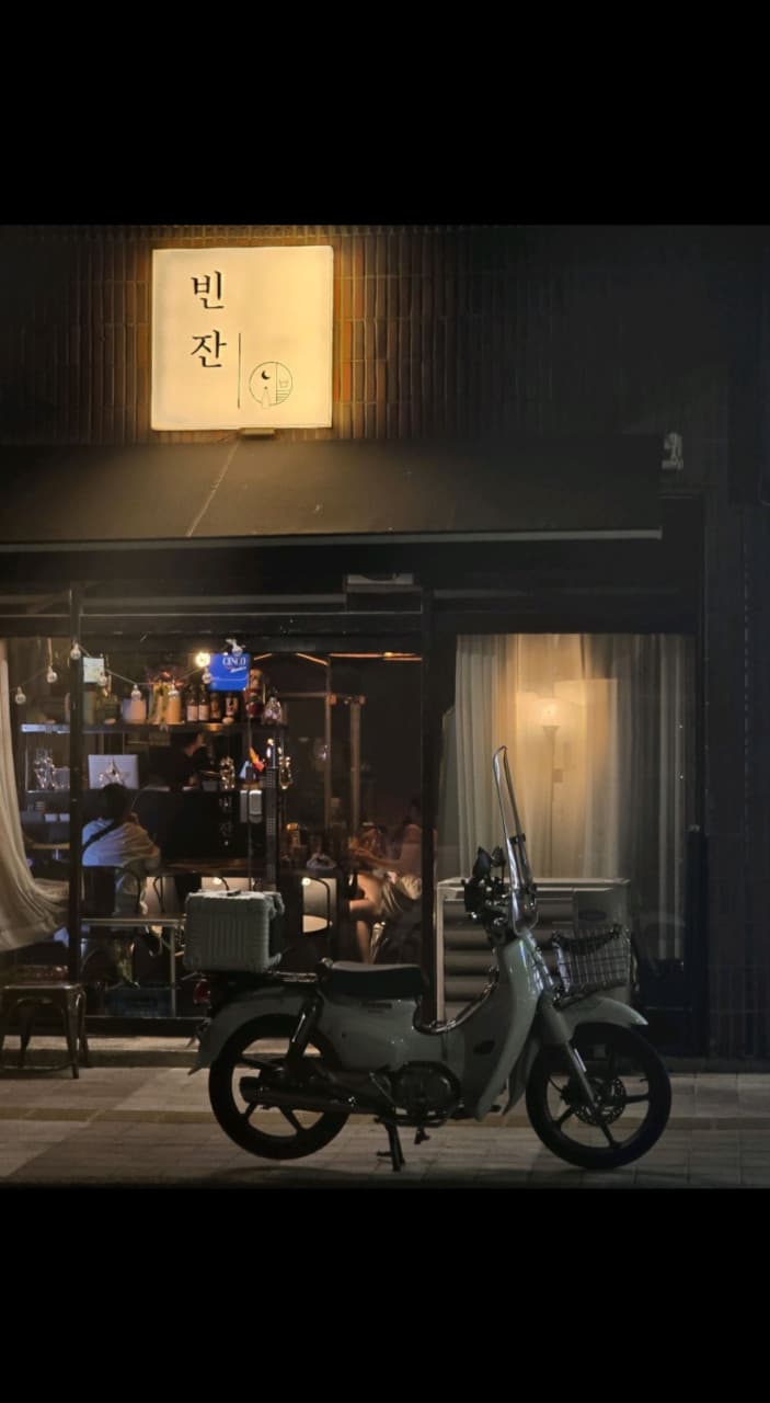 충청북도 충주시 빈잔 맥주 호프 매장 전경. 노란 조명 아래 다찌석에서 혼술을 즐기는 사람들과 전면 유리창 앞에 주차된 하얀색 스쿠터가 보이는 밤의 풍경.