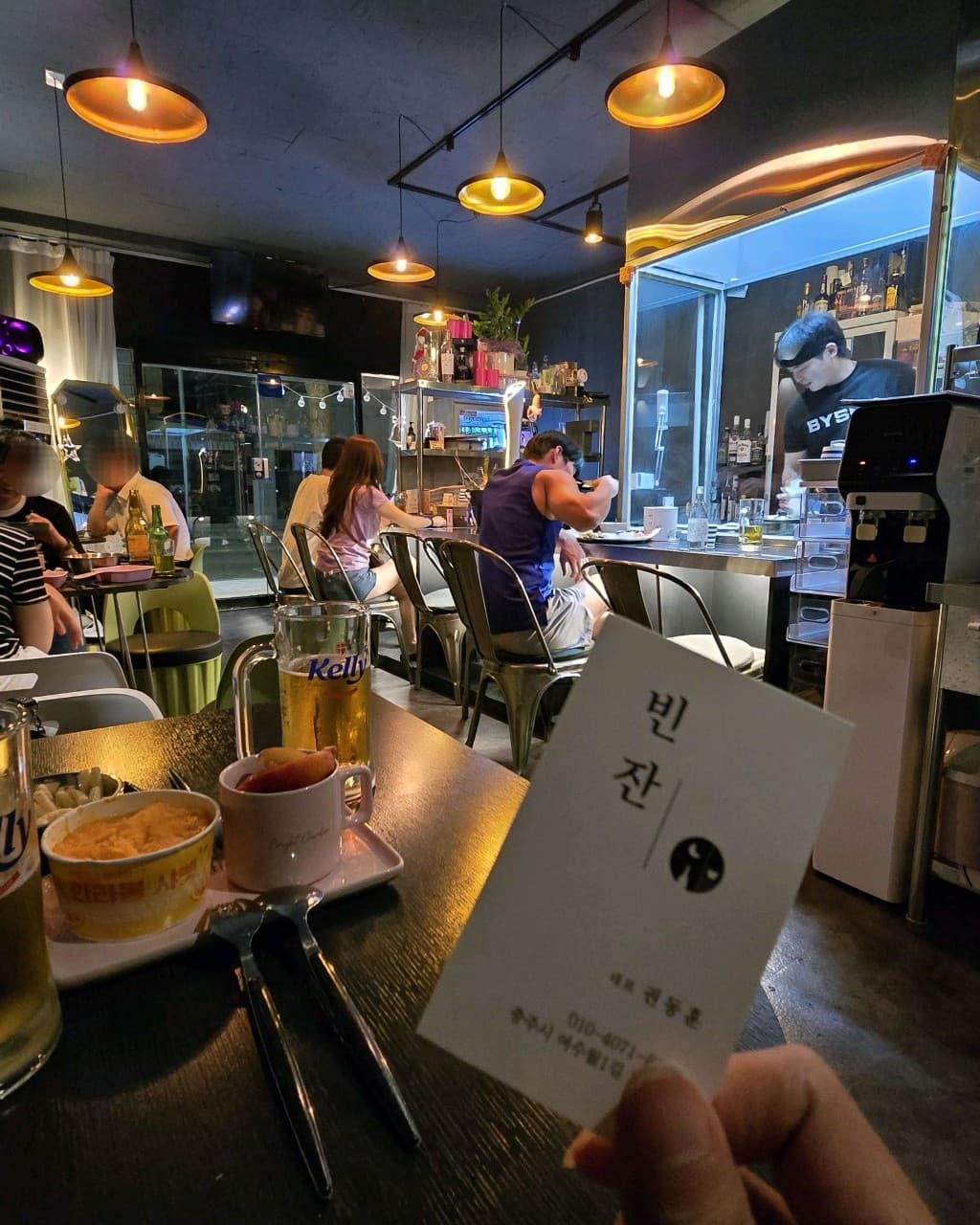 충청북도 충주시 빈잔 맥주 호프. 노란 펜던트 조명 아래 다찌석에서 혼술하는 손님과 테이블 위 생맥주. 1인석과 카운터 자리가 마련된 매장 내부 전경.