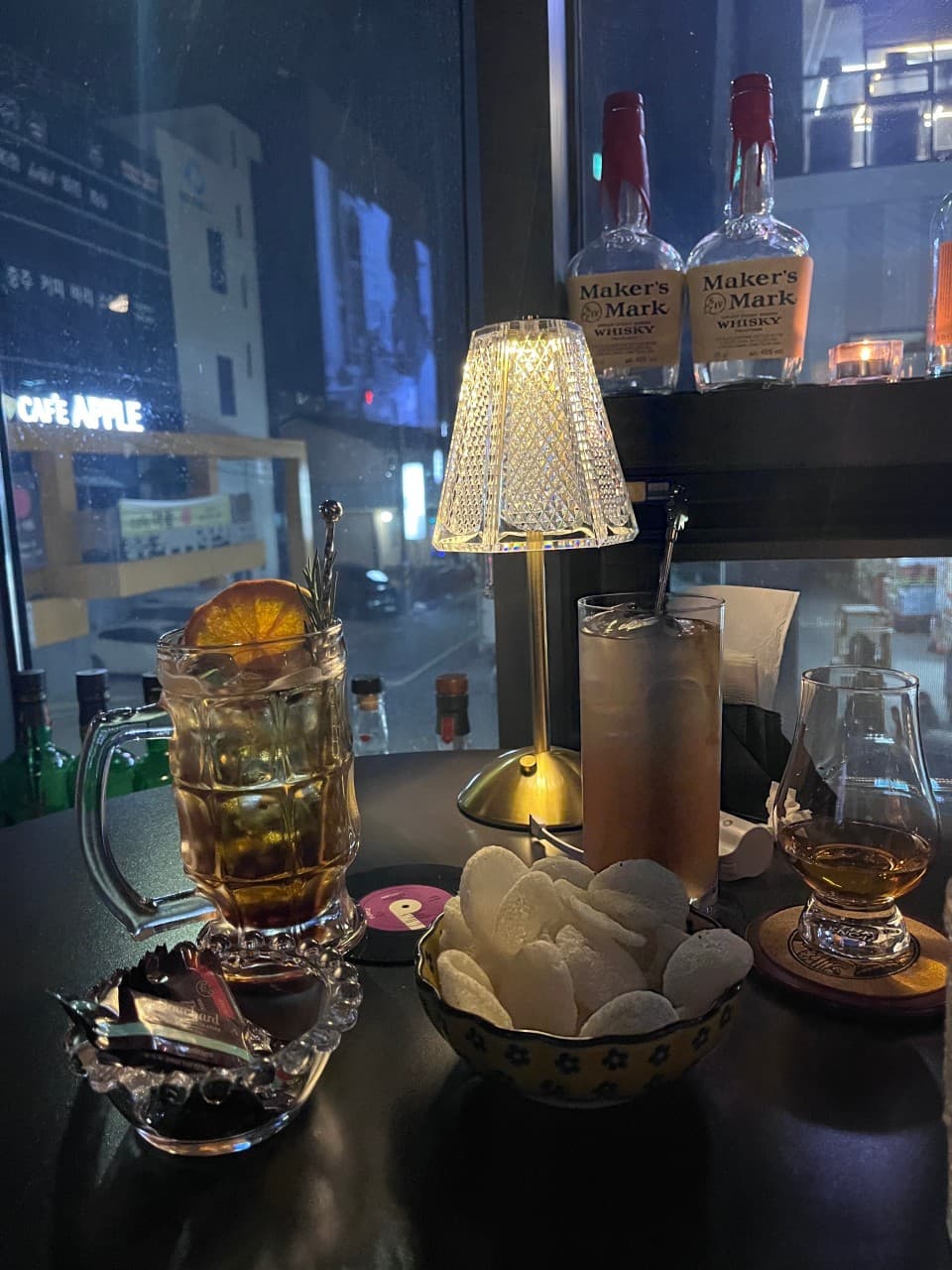 충청북도 충주시 바(Bar) 조용의 창가 1인석 테이블. 하이볼 속 오렌지 슬라이스와 바삭한 스낵이 노란 핀 조명 아래 놓인 혼술 현장.