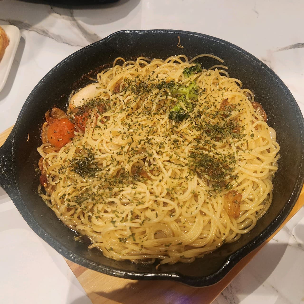 충청북도 충주시 킹덤투하츠 와인바 - 무쇠 팬에 담긴 1인 오일 파스타와 마늘 토마토의 질감. 대리석 테이블 위 조명이 비치는 다찌석 혼술 상황
