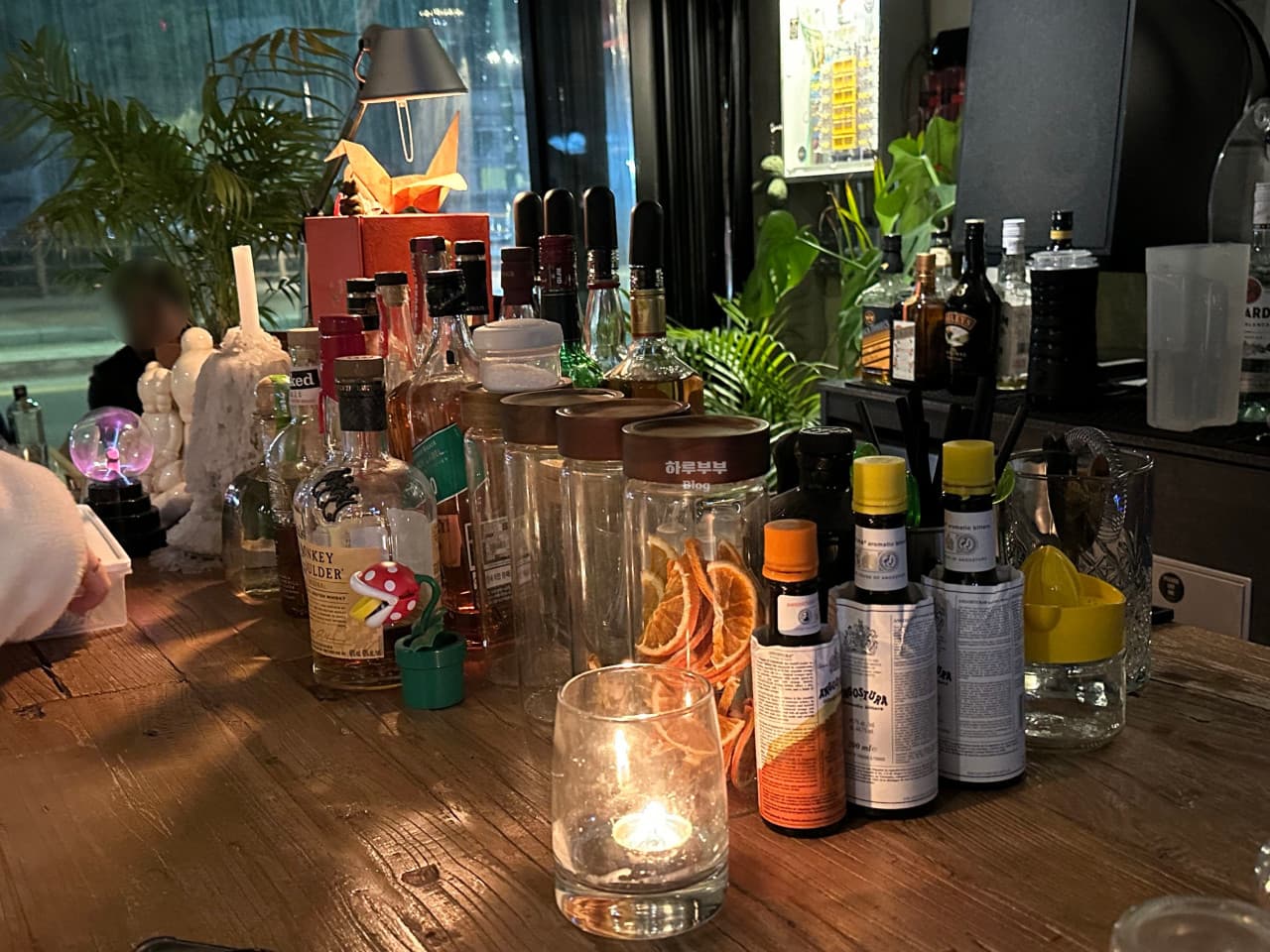 충청북도 충주시 매드슬로우 용산 바(Bar)의 목재 다찌석 위 촛불과 위스키 병. 말린 과일 가니쉬와 비터스가 놓여 있는 1인 혼술 공간의 배치.